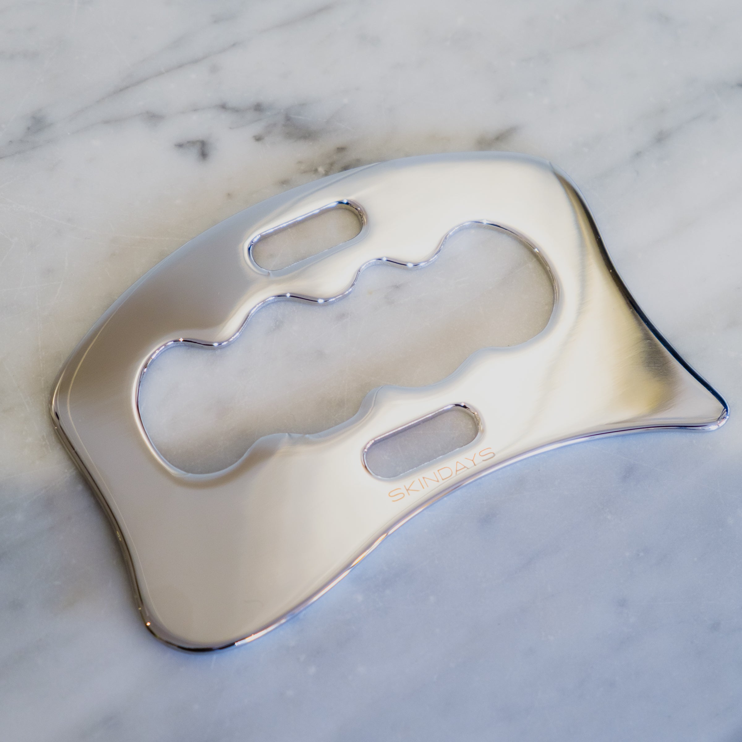 Skindays Body Gua Sha in polished stainless steel on marble surface