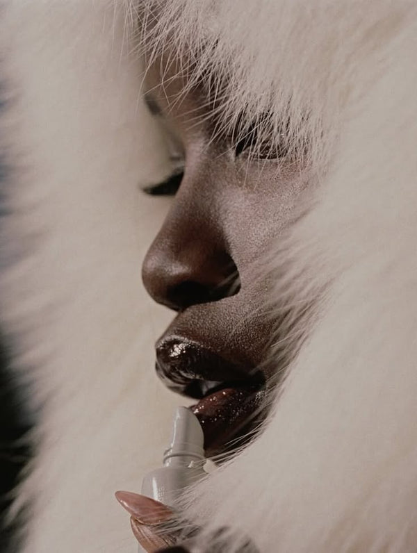 Close-up of a face in a cream fur hood applying lip gloss