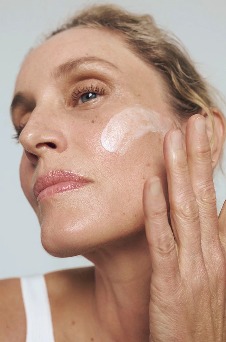 Close up of a mature woman applying a swipe of cream to her cheek