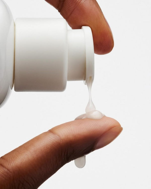 A drop of white lotion falling from a pump bottle onto a fingertip